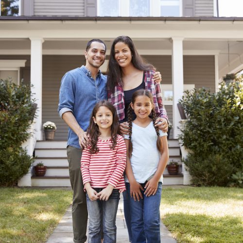 Portrait Of Smiling Family Standing In Front Of Their Home